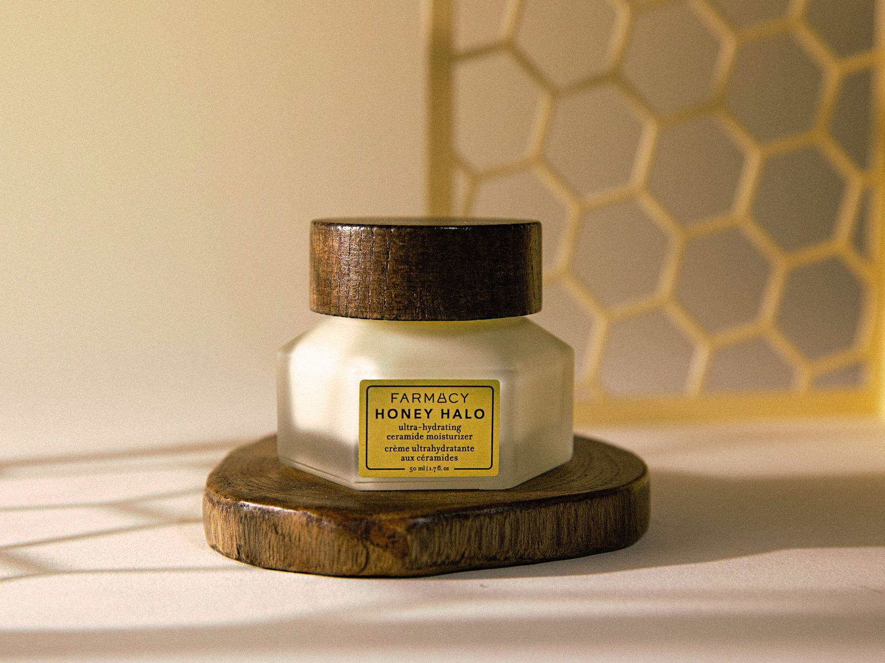 Farmacy Honey Halo jar on a wood slice with a honeycomb screen and warm sunlight.