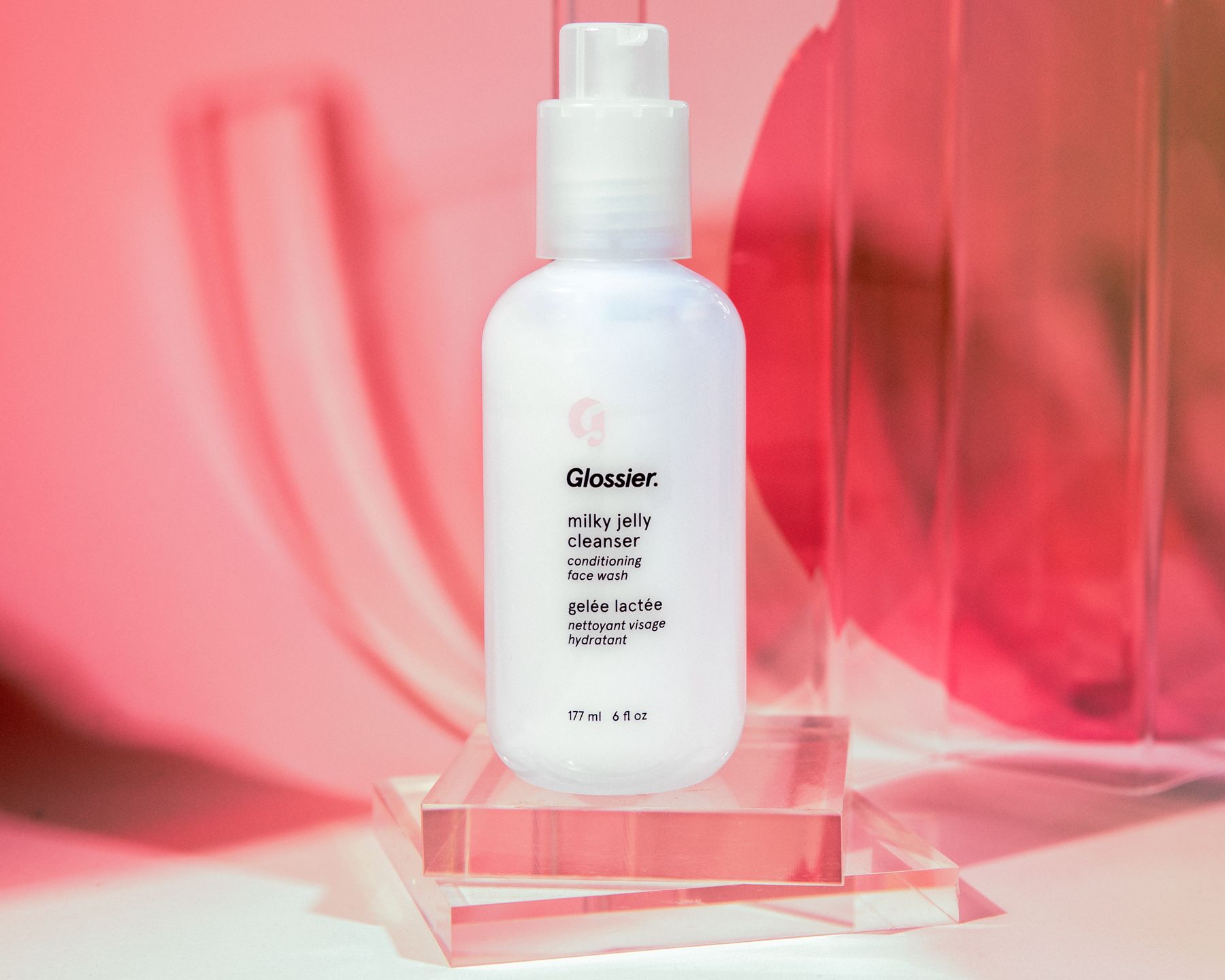 Glossier Milky Jelly Cleanser on pink acrylic with red/pink light.