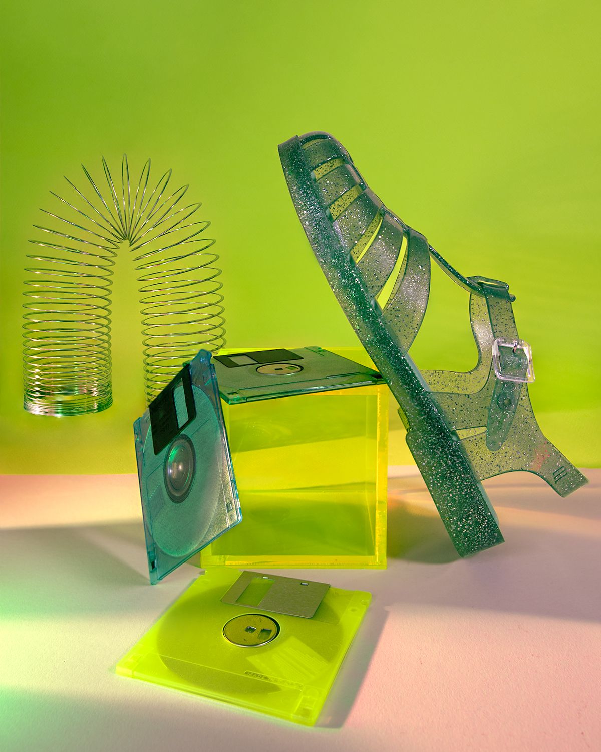 Green jelly sandal, Slinky, floppy disk and neon acrylic cube on lime/pink.