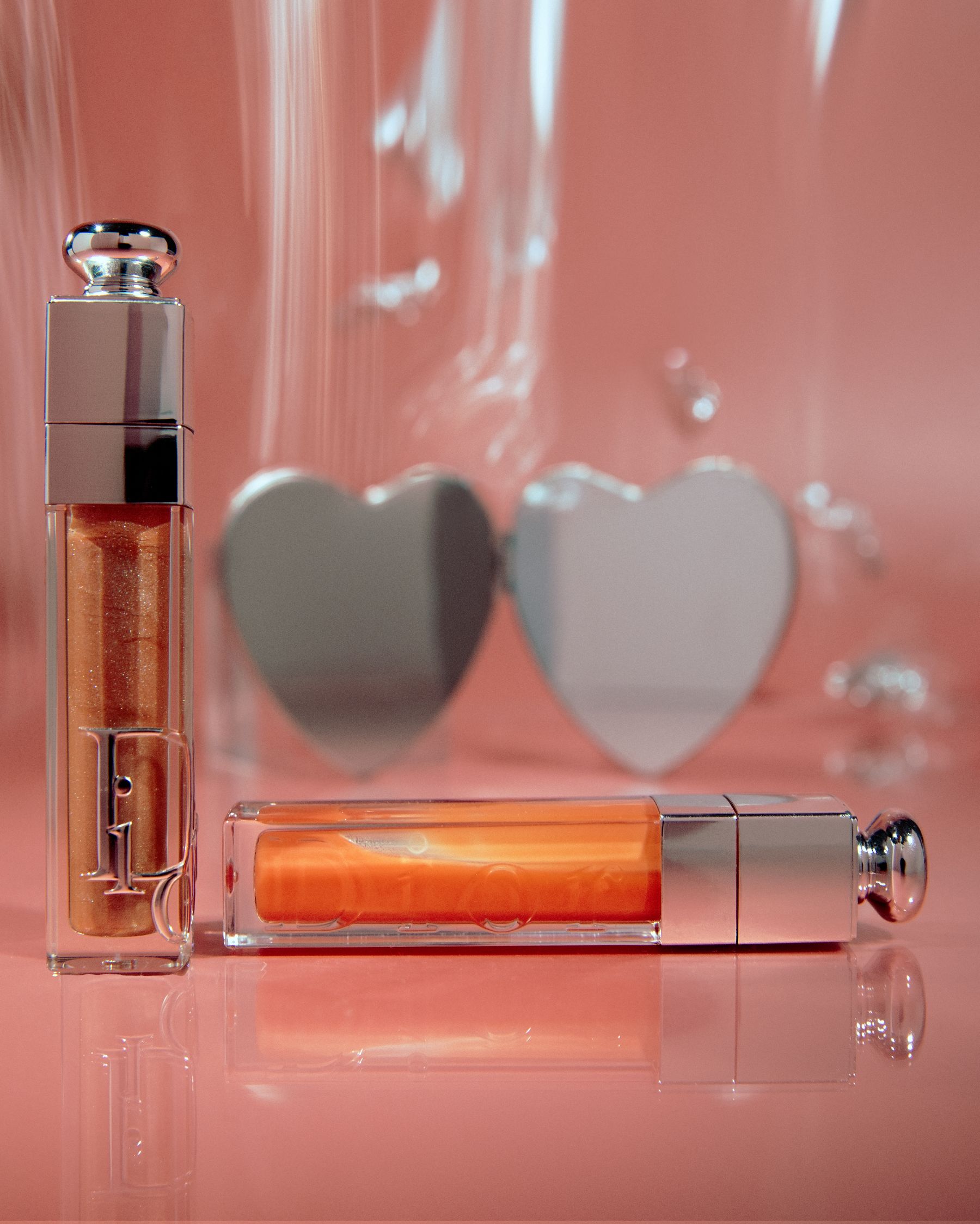 Two orange-tint lip-oil tubes with heart-shaped mirrors on pink acrylic.