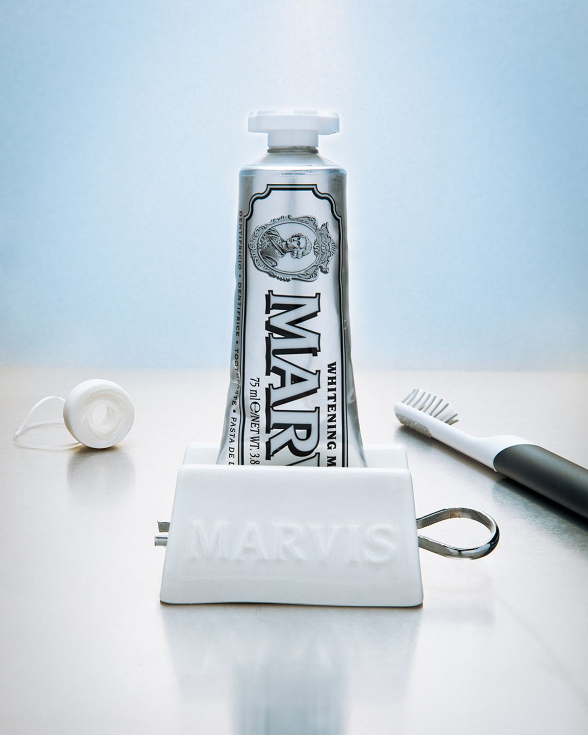 Marvis toothpaste tube in a white Marvis stand beside an electric toothbrush, cool light.