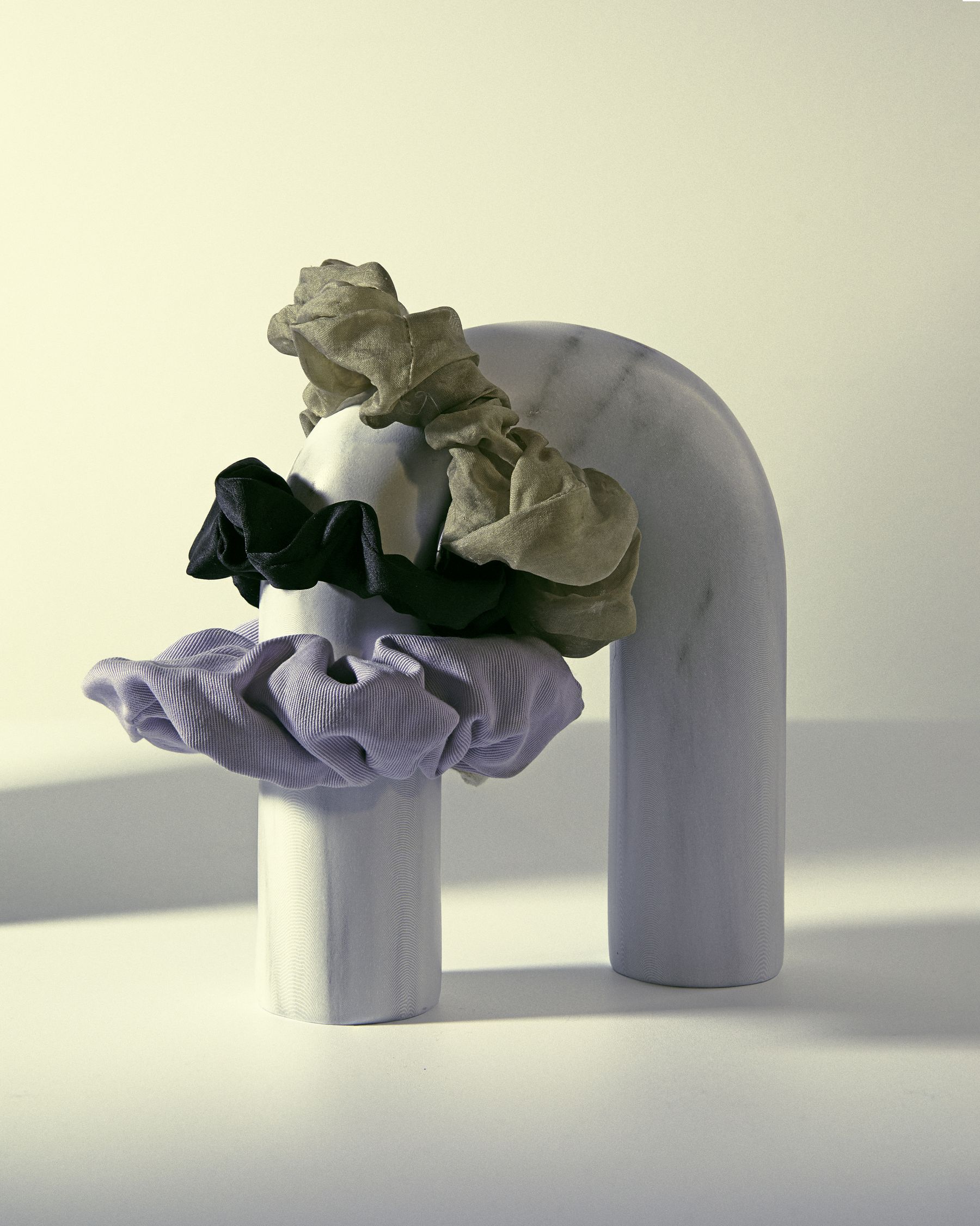 Scrunchies (olive, black, lilac) draped on a white marble arch sculpture.