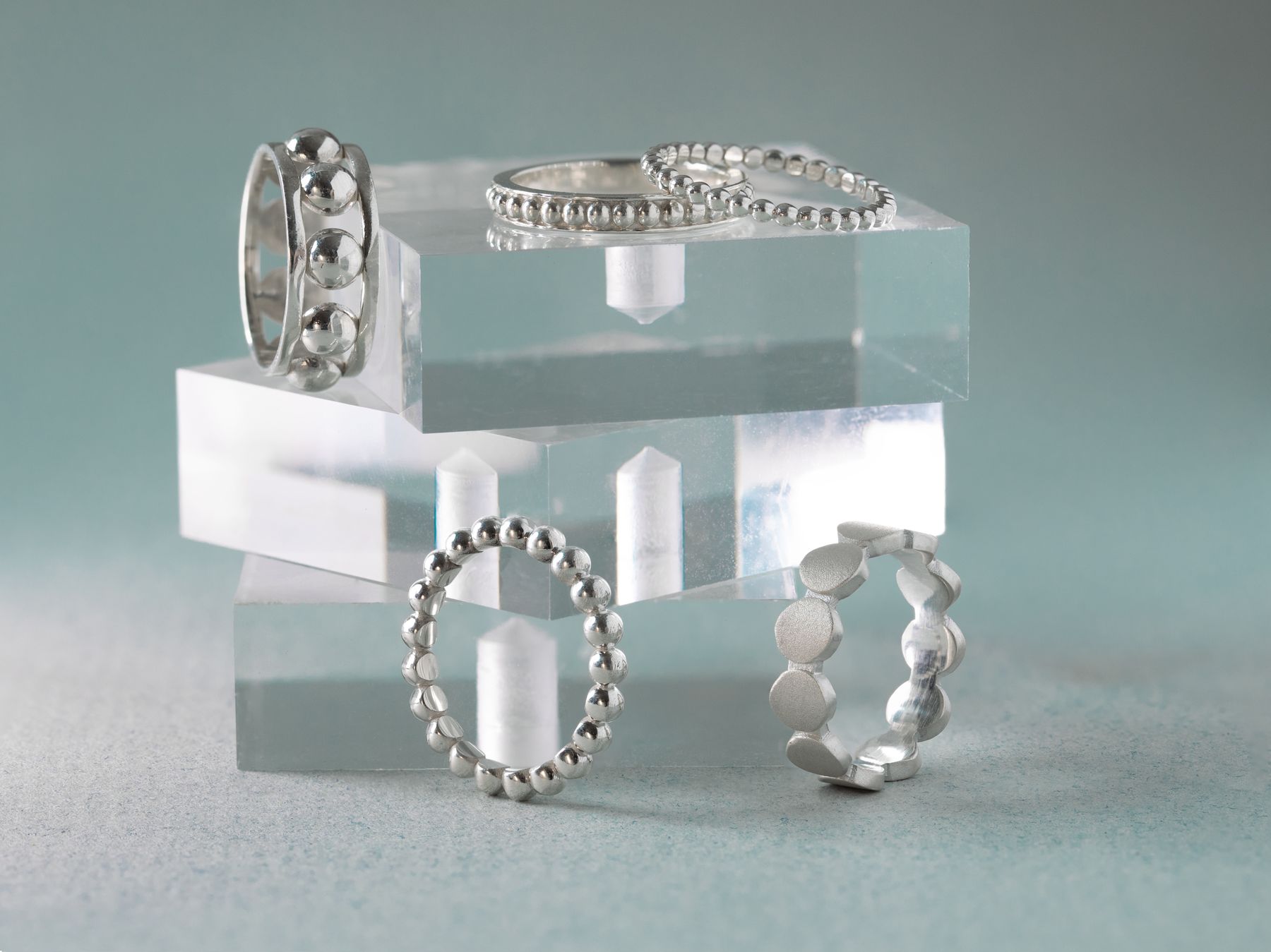 Silver rings displayed on clear acrylic blocks, soft grey.