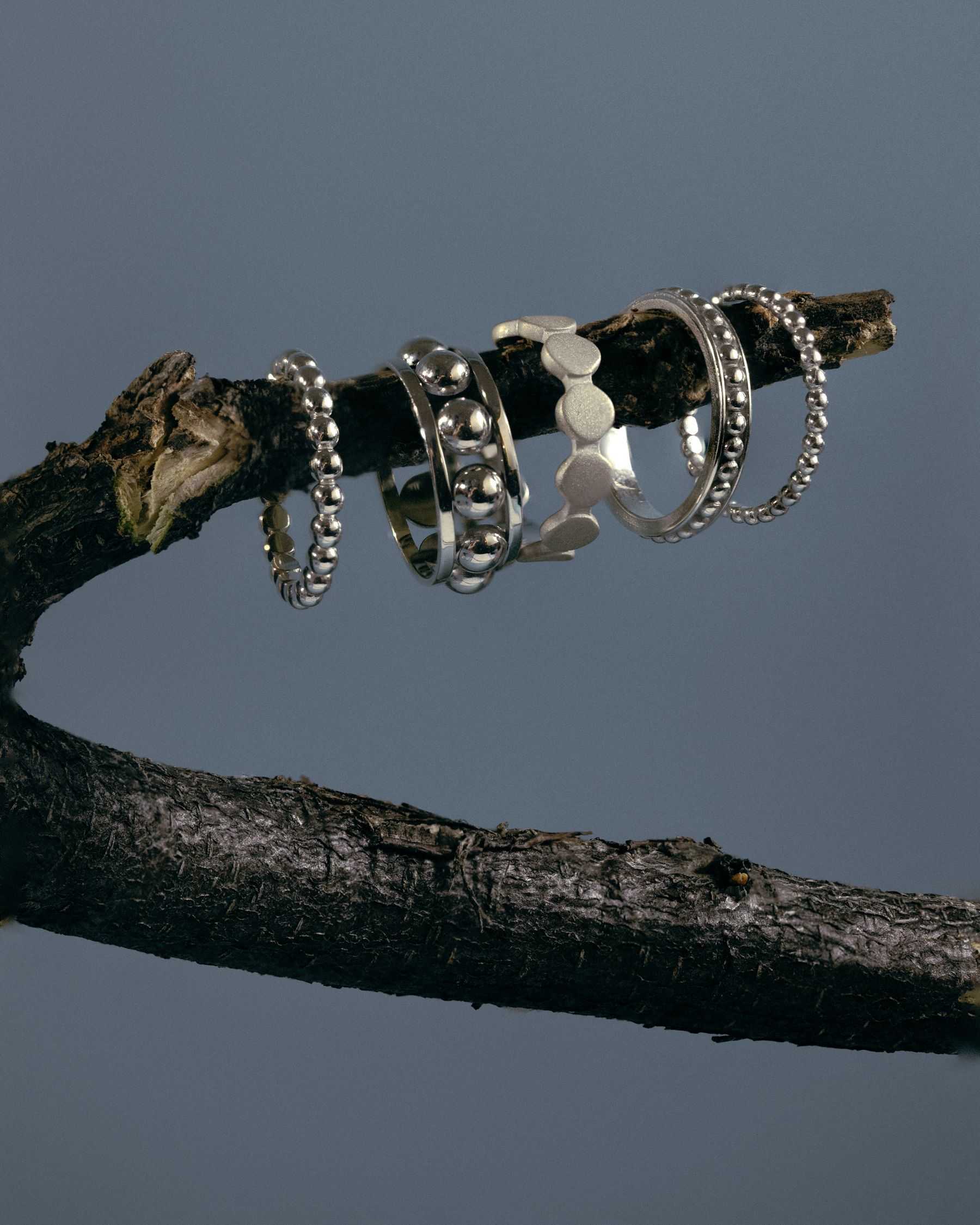 Silver rings stacked on a dark branch against slate blue.