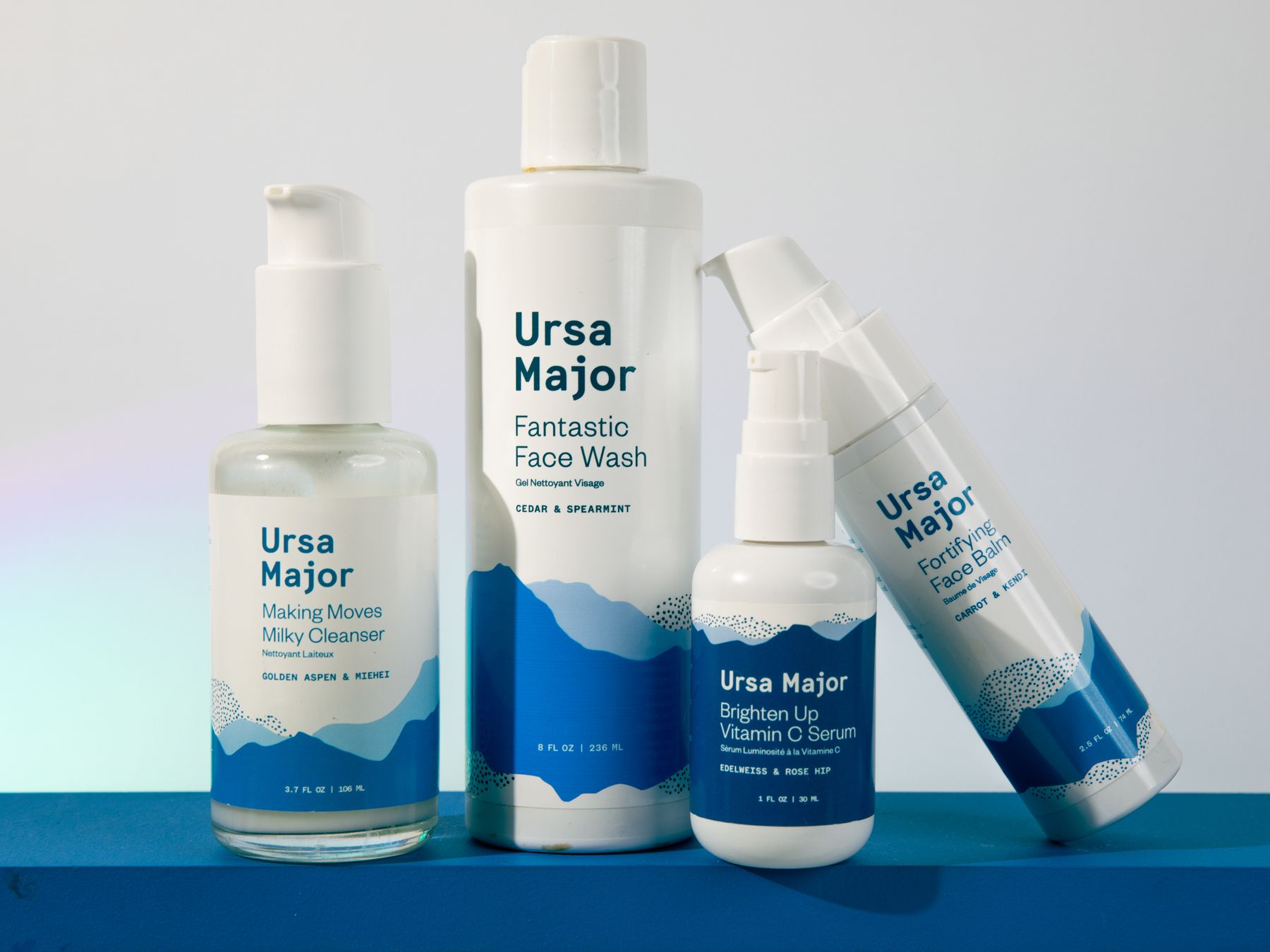 Ursa Major skincare line-up (face wash, cleanser, serums) on a blue step.