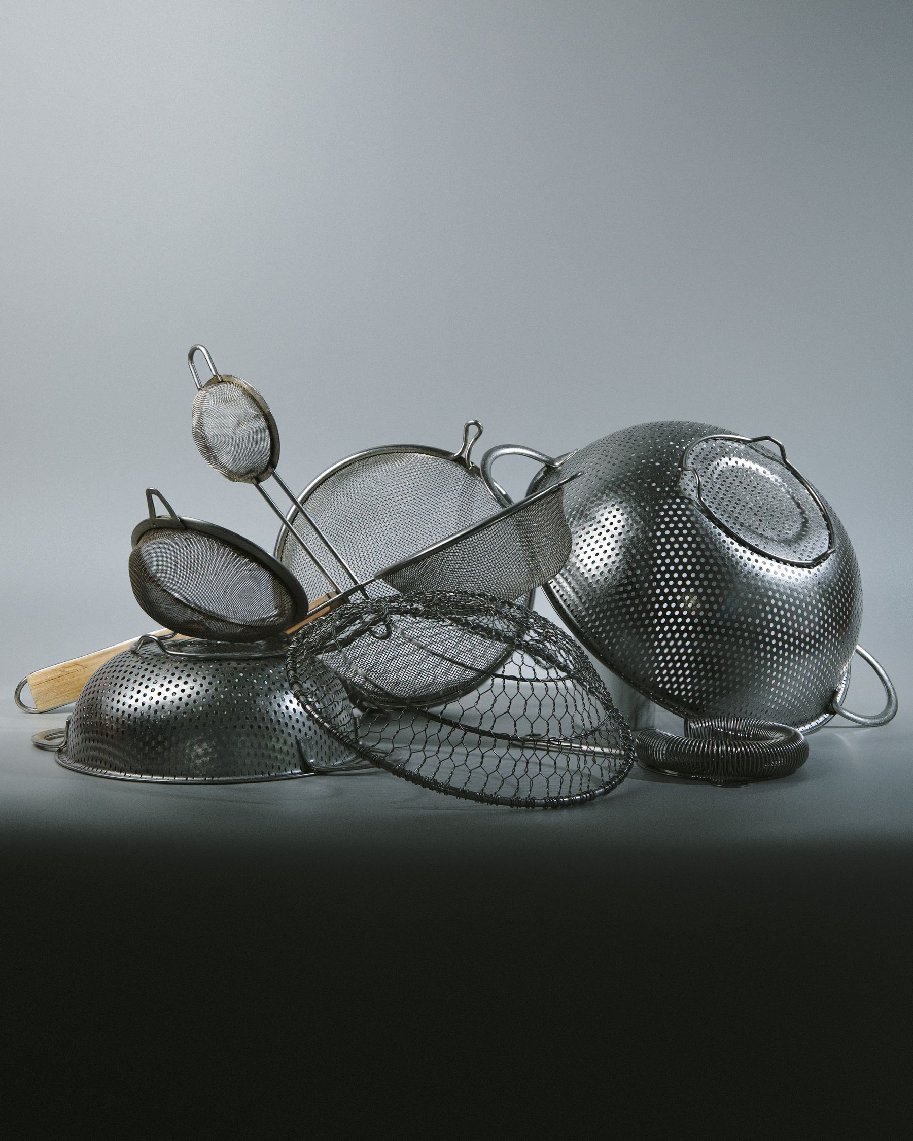 Stacked metal strainers and sieves on moody grey.