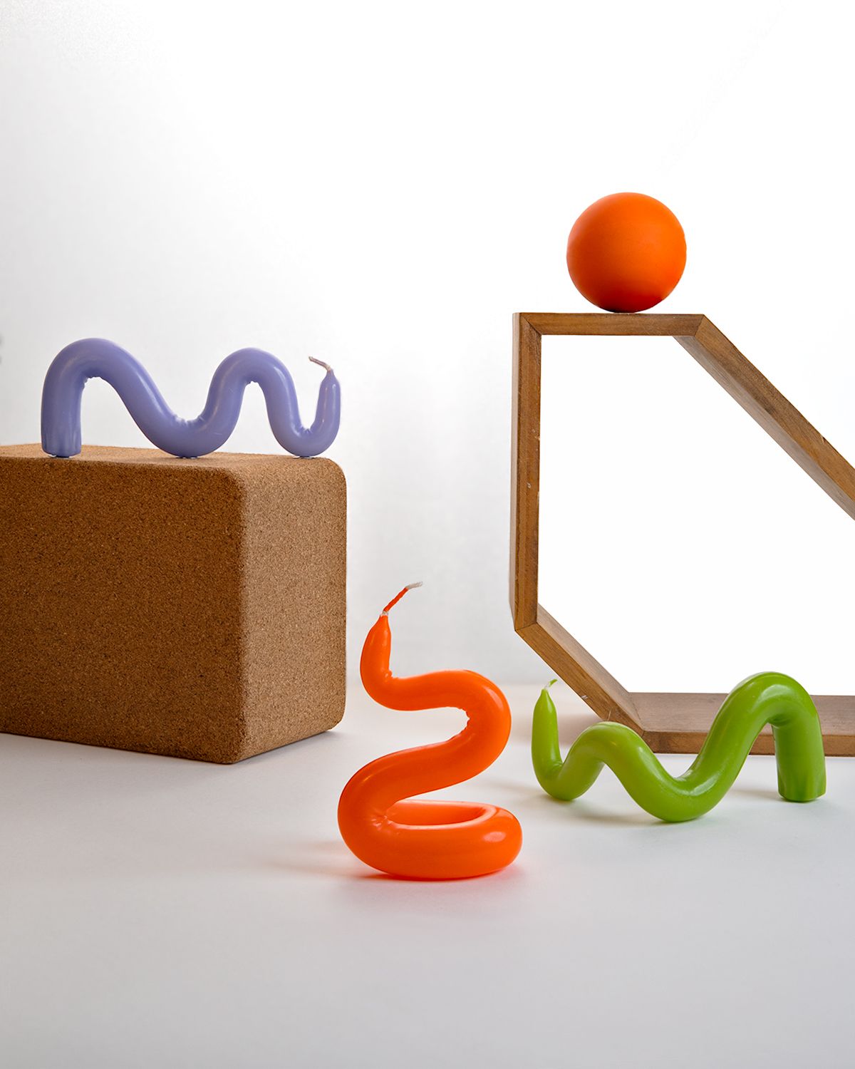 Playful set: lilac, orange and green squiggle forms, cork block, wooden hexagon frame and an orange ball on white.