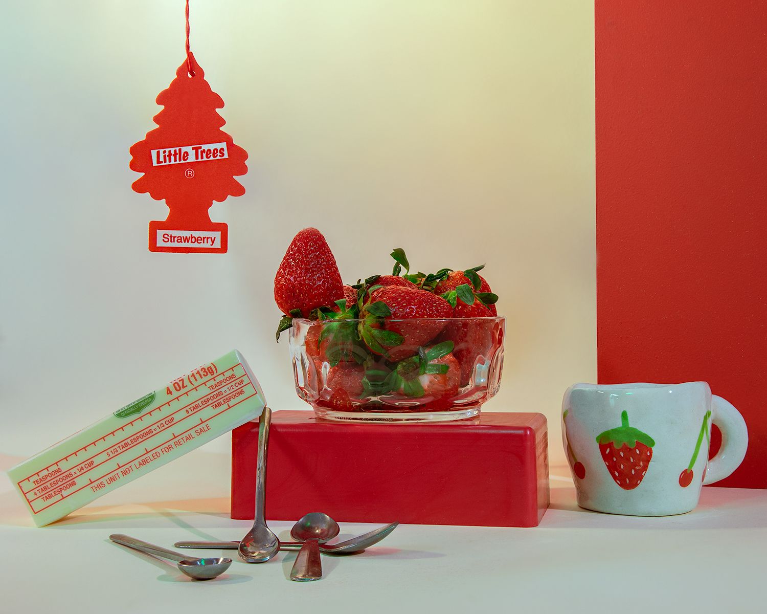 Strawberry-themed set: strawberry air freshener, bowl of strawberries, strawberry mug, spoons and red blocks.