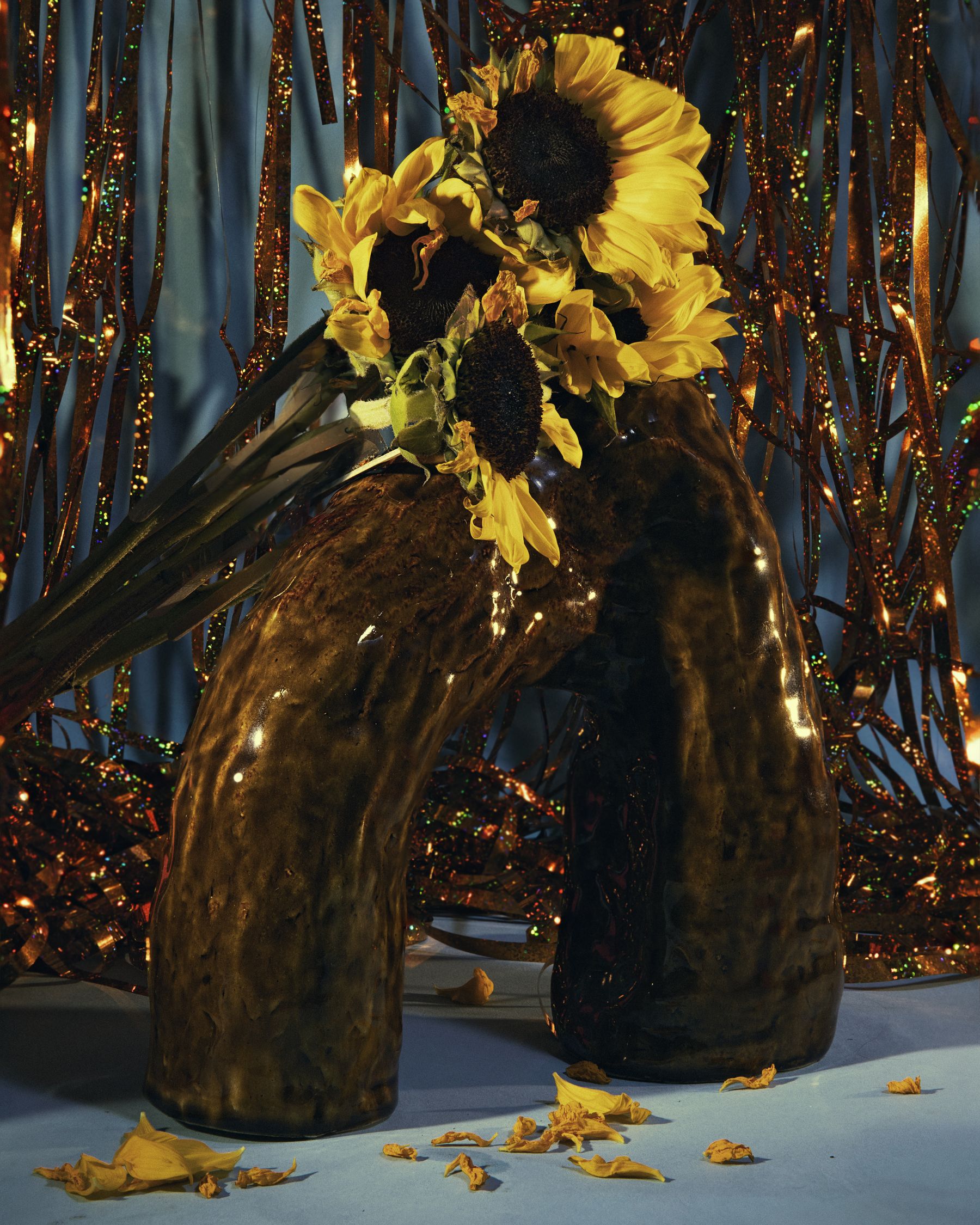 Sunflowers in amber glass vases against gold tinsel curtain.
