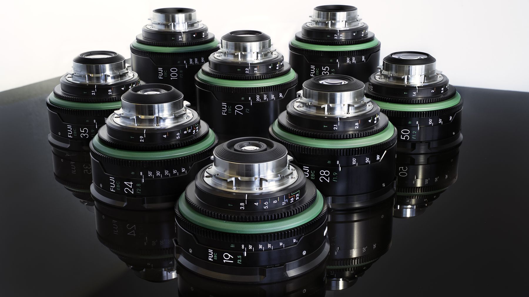 Cluster of cine lenses with green rings on a glossy black surface.