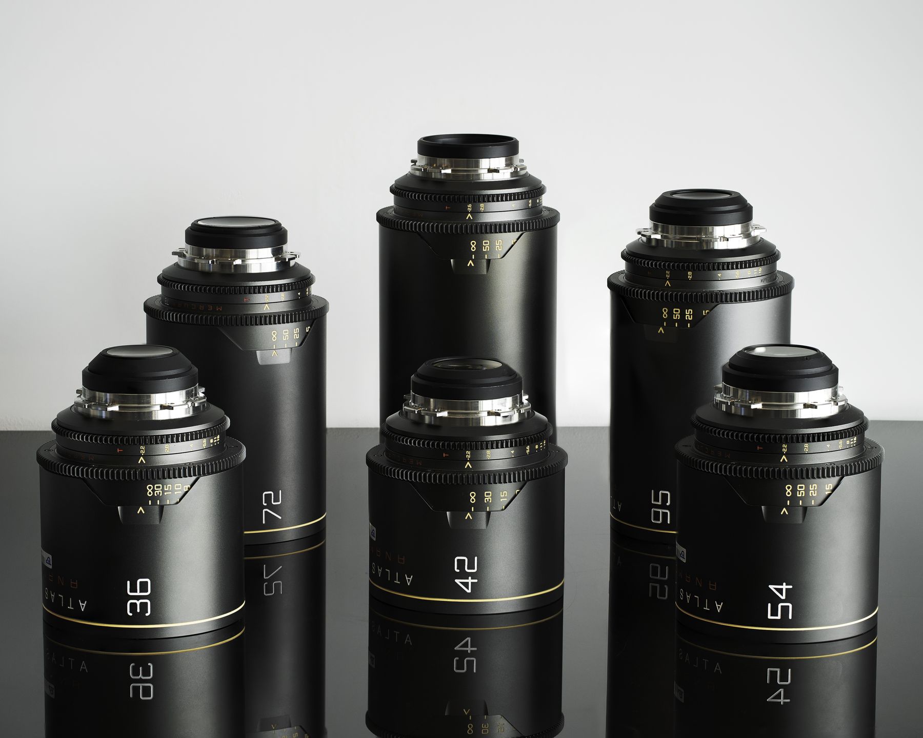 Set of black cine prime lenses standing on a reflective surface, white backdrop.