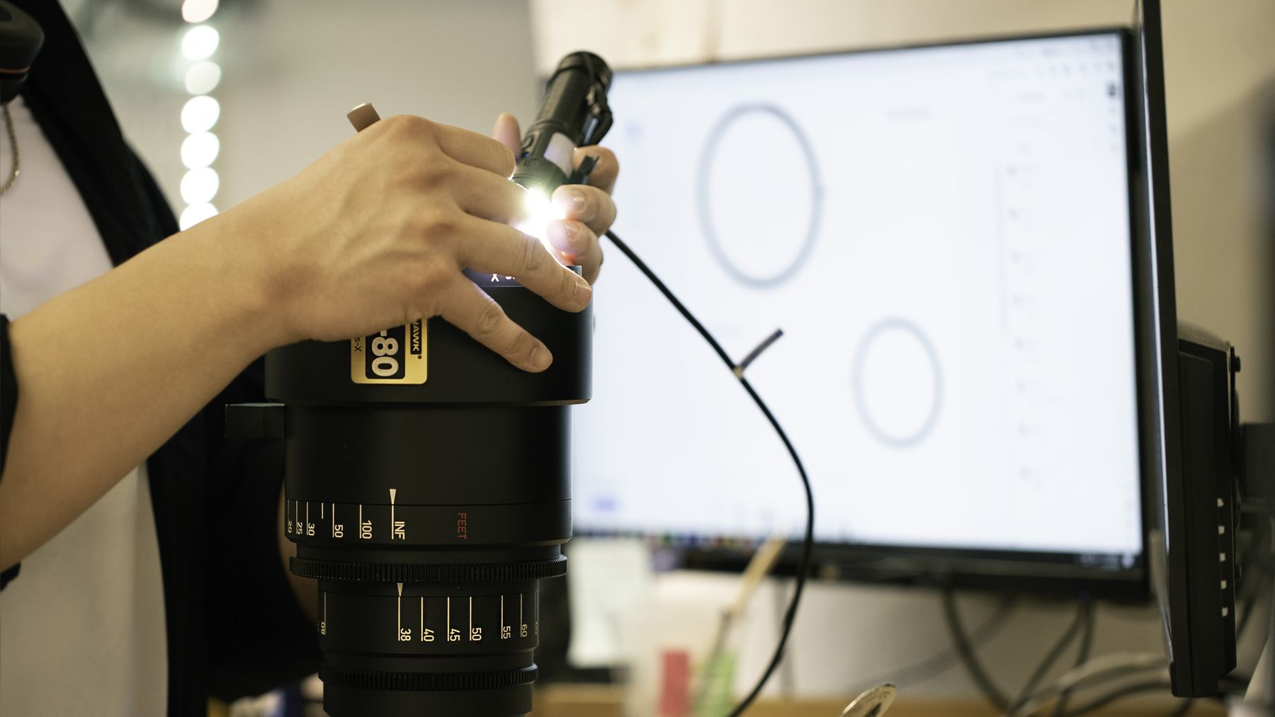 Technician inspecting a lens with a lit projector and monitor.