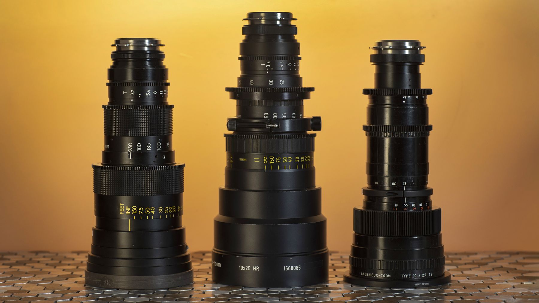 Three zoom lenses standing side by side, amber backdrop.