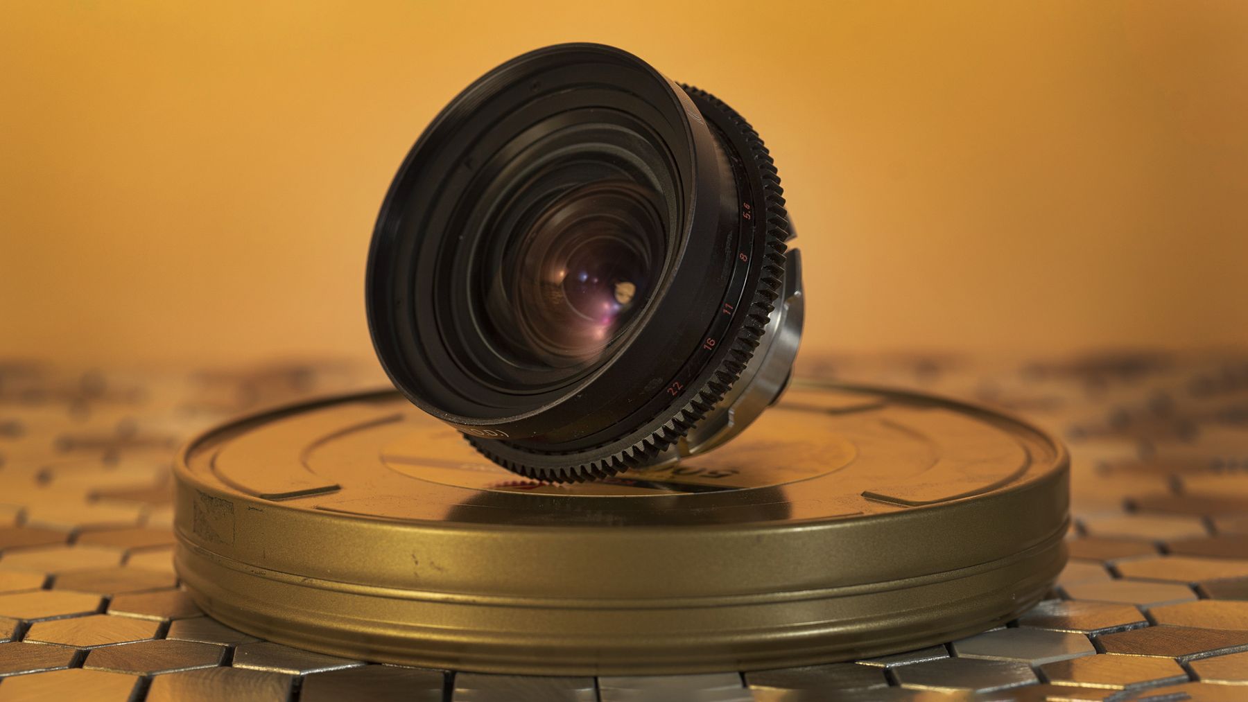 Vintage lens resting on a brass film can, amber backdrop.
